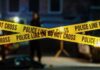Police tape marking a crime scene with blurred figures in the background