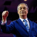 A man in a blue suit raising his fist confidently on stage