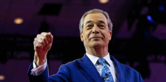 A man in a blue suit raising his fist confidently on stage