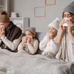 A family of four sitting on a couch, all looking unwell and using tissues