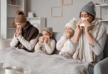 A family of four sitting on a couch, all looking unwell and using tissues