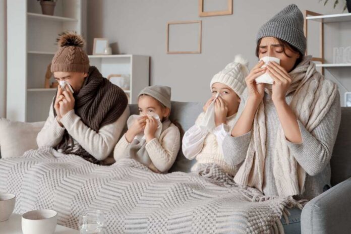 A family of four sitting on a couch, all looking unwell and using tissues