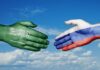 A green hand representing Saudi Arabia and a white hand representing Russia reaching out for a handshake against a blue sky