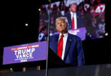 A man in a suit stands at a podium with a microphone during a political rally