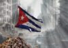 Tattered Cuban flag waving over a pile of rubble in a devastated urban landscape