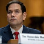 A government official sitting at a hearing with a serious expression
