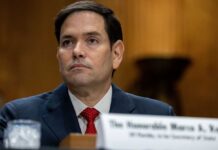 A government official sitting at a hearing with a serious expression