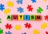 Colorful blocks spelling 'AUTISM' surrounded by puzzle pieces on a pink background