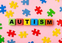 Colorful blocks spelling 'AUTISM' surrounded by puzzle pieces on a pink background