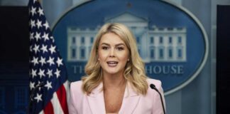 A government official speaking at a press briefing in front of the White House backdrop