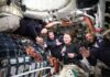 Four astronauts in a spacecraft, smiling and giving thumbs up