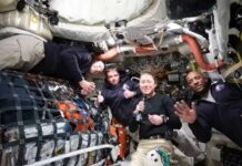 Four astronauts in a spacecraft, smiling and giving thumbs up
