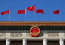 Chinese flags and national emblem displayed on a government building against a blue sky