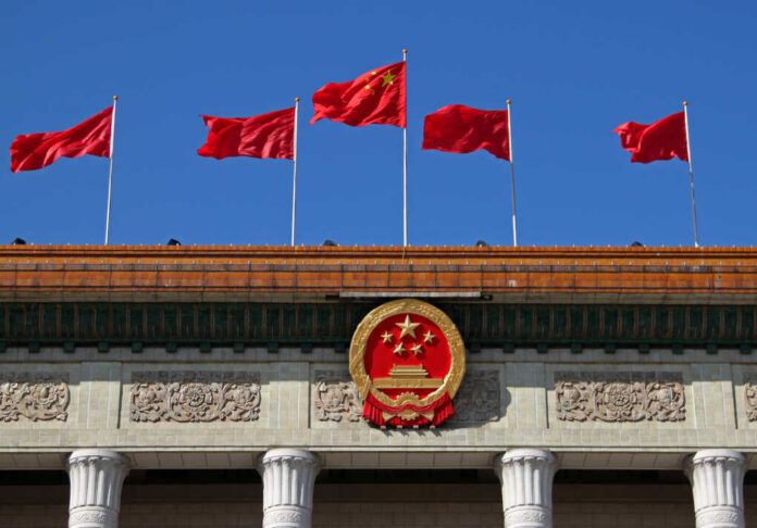 Chinese flags and national emblem displayed on a government building against a blue sky