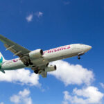 An airplane flying through a clear blue sky with clouds