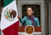 A government official delivering a speech in front of the Mexican flag