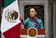 A government official delivering a speech in front of the Mexican flag