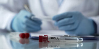Ebola test tube on lab table with gloved researcher in background