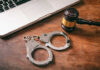 Handcuffs and a gavel placed next to a laptop on a wooden surface