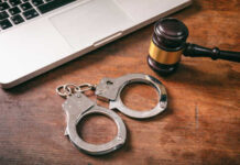 Handcuffs and a gavel placed next to a laptop on a wooden surface