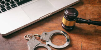 Handcuffs and a gavel placed next to a laptop on a wooden surface