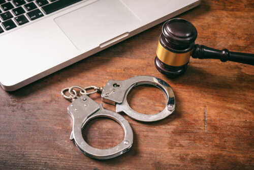 Handcuffs and a gavel placed next to a laptop on a wooden surface