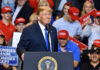 A speaker at a political rally smiling in front of an enthusiastic crowd wearing red hats