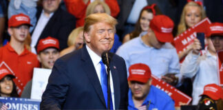 A speaker at a political rally smiling in front of an enthusiastic crowd wearing red hats