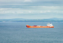 An orange cargo ship sailing in the ocean with a coastal landscape in the background