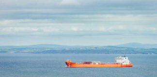 An orange cargo ship sailing in the ocean with a coastal landscape in the background