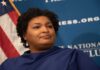 Abrams’ Political Future at Risk – Subpoena Drama! A political figure speaking at a podium with a blue backdrop