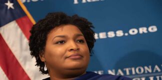 A political figure speaking at a podium with a blue backdrop