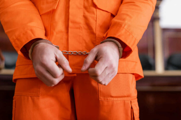 shutterstock_2121704996 A person in an orange jumpsuit with handcuffs