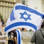 Spa Boots Jews Over Star Necklace? Person holding an Israeli flag at a public demonstration