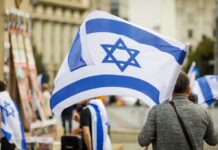 Spa Boots Jews Over Star Necklace? Person holding an Israeli flag at a public demonstration