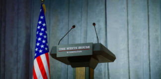 Press podium with microphones and American flag in the background