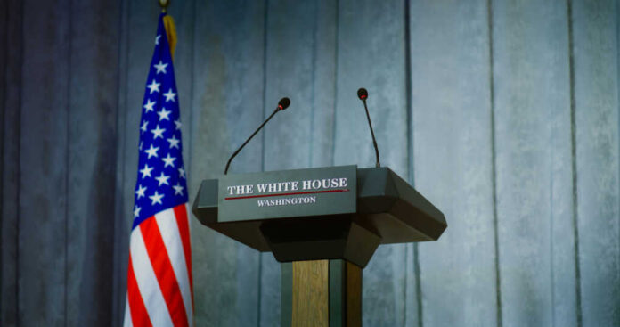 Press podium with microphones and American flag in the background