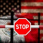 Disturbing Discovery at US-Mexico Border! Stop sign on barrier with blurred U.S. and Mexico flags behind fence