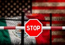 Disturbing Discovery at US-Mexico Border! Stop sign on barrier with blurred U.S. and Mexico flags behind fence