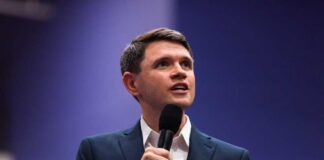 A man in a suit speaking into a microphone at a conference