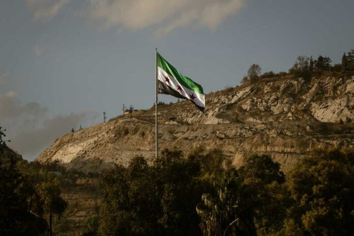Syrian flag waving in front of a mountainous landscape