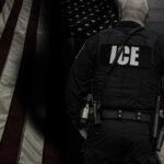 ICE agent standing in front of an American flag