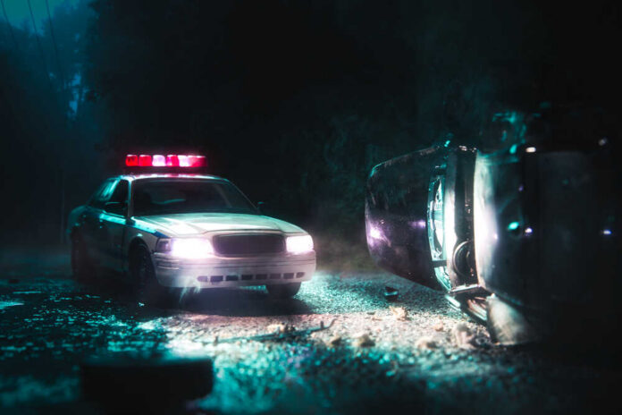 A police car with flashing lights at the scene of a flipped vehicle accident
