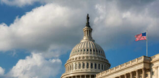 The U.S. Capitol building with a dome and an American flag under a cloudy sky