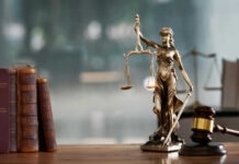 A bronze statue of Lady Justice holding scales and a sword, with law books and a gavel in the foreground