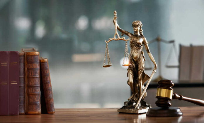 A bronze statue of Lady Justice holding scales and a sword, with law books and a gavel in the foreground