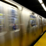 A subway train in motion at a station with a yellow platform