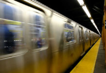 A subway train in motion at a station with a yellow platform