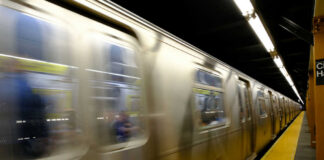 A subway train in motion at a station with a yellow platform