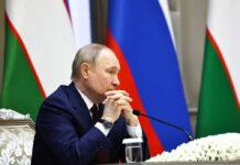 A government official sitting at a conference table with a serious expression